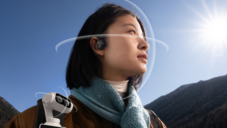 Image of a woman with the POV Head Tracker mounted on the Ear Mount in her ear, using it to control her Stellar White Insta360 Luna Ultra gimbal camera, which is mounted on her bag strap using the Backback Mount.